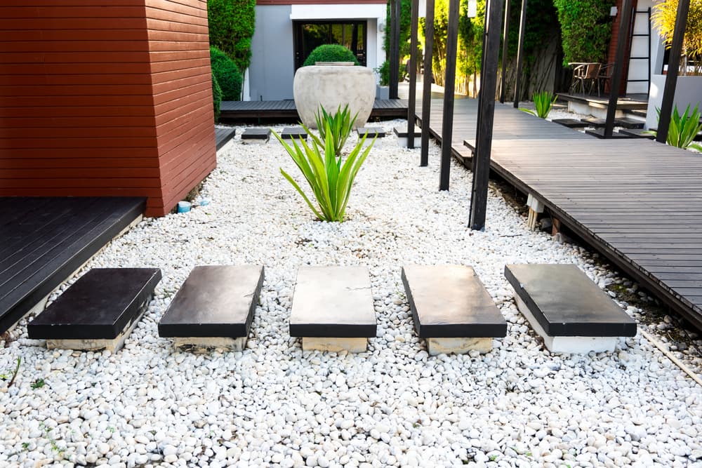 Black rocks walking way in tropical garden, Black stones garden path on white pebbles and lush green trees, Garden decoration concept